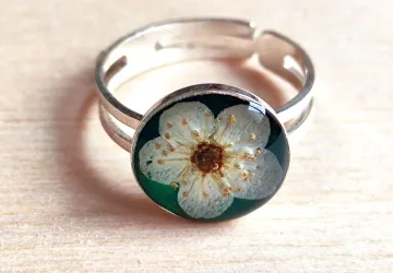 Anillo de plata 925 con base de bio resina pigmentada en verde esmeralda y flor de corona de novia. 