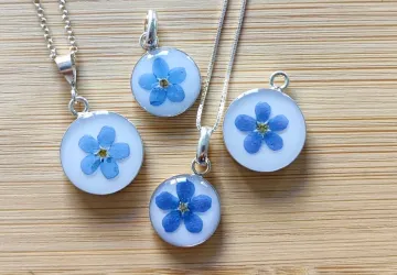 Colgantes mini con fonde blanco de resina pigmentada, flor Nomeolvides y base de plata. Collares tipo medalla. 