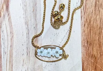 Pulsera de acero inoxidable dorado con bisel tipo oval y cadena de cierre fácil. En el bisel hay tres pequeñas flores blancas encapsuladas